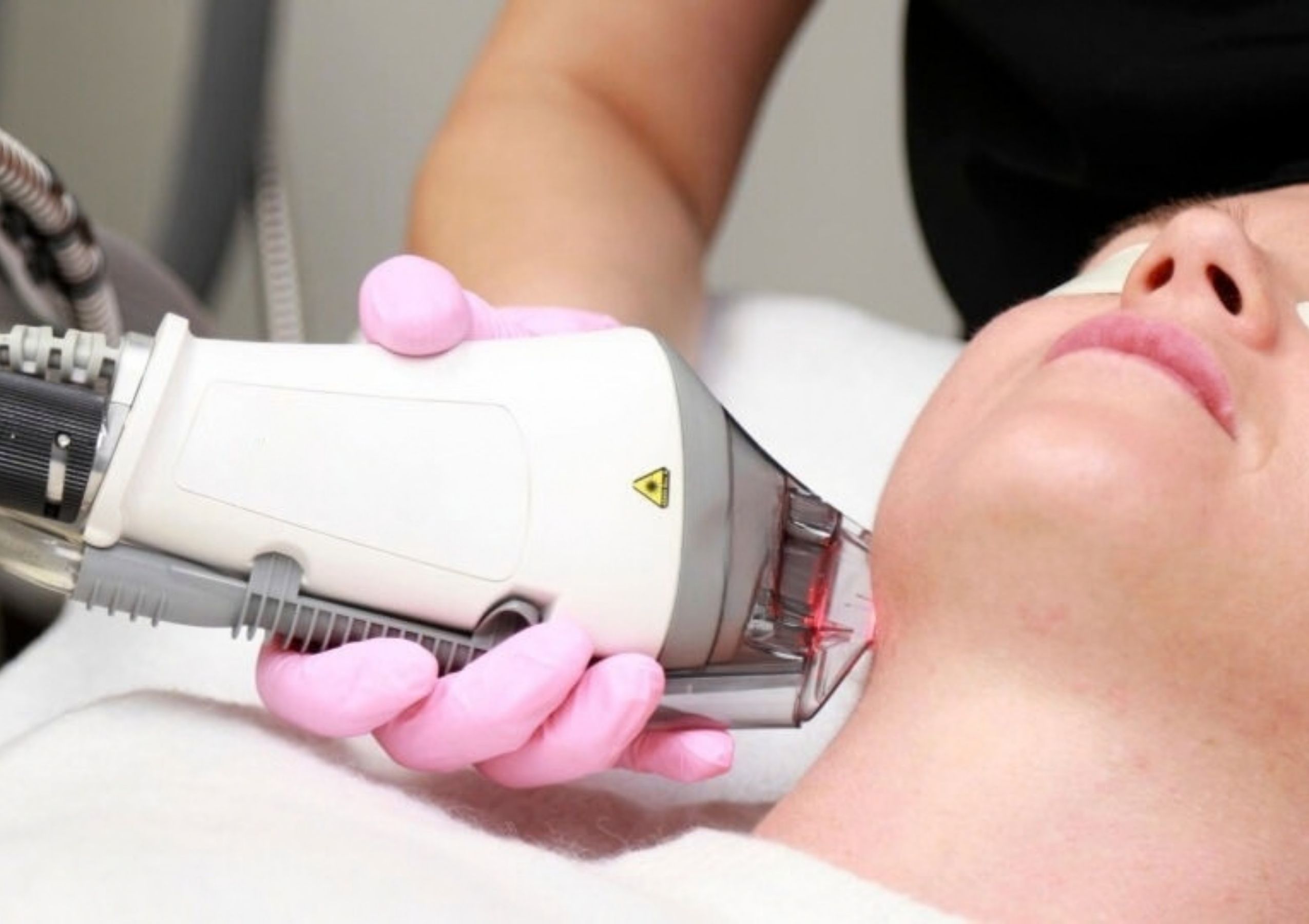 Clinician in gloves uses a handheld device on a patient’s cheek during a cosmetic facial treatment.